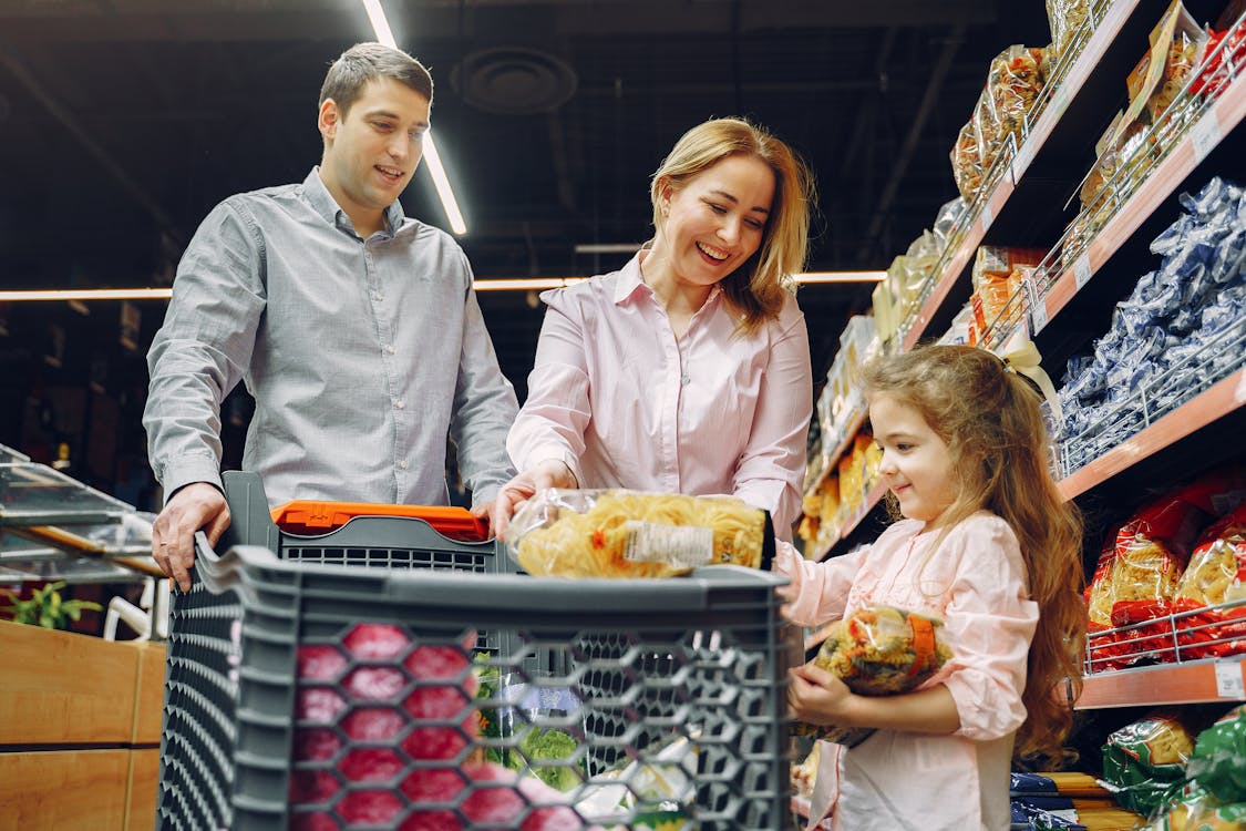 young child putting groceries in cart with parents watching