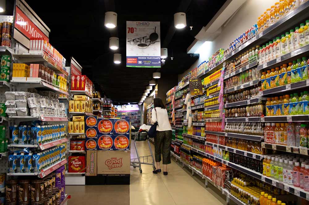 Inside of a grocery store with stocked products and a women with cart standing in between multiple aisles