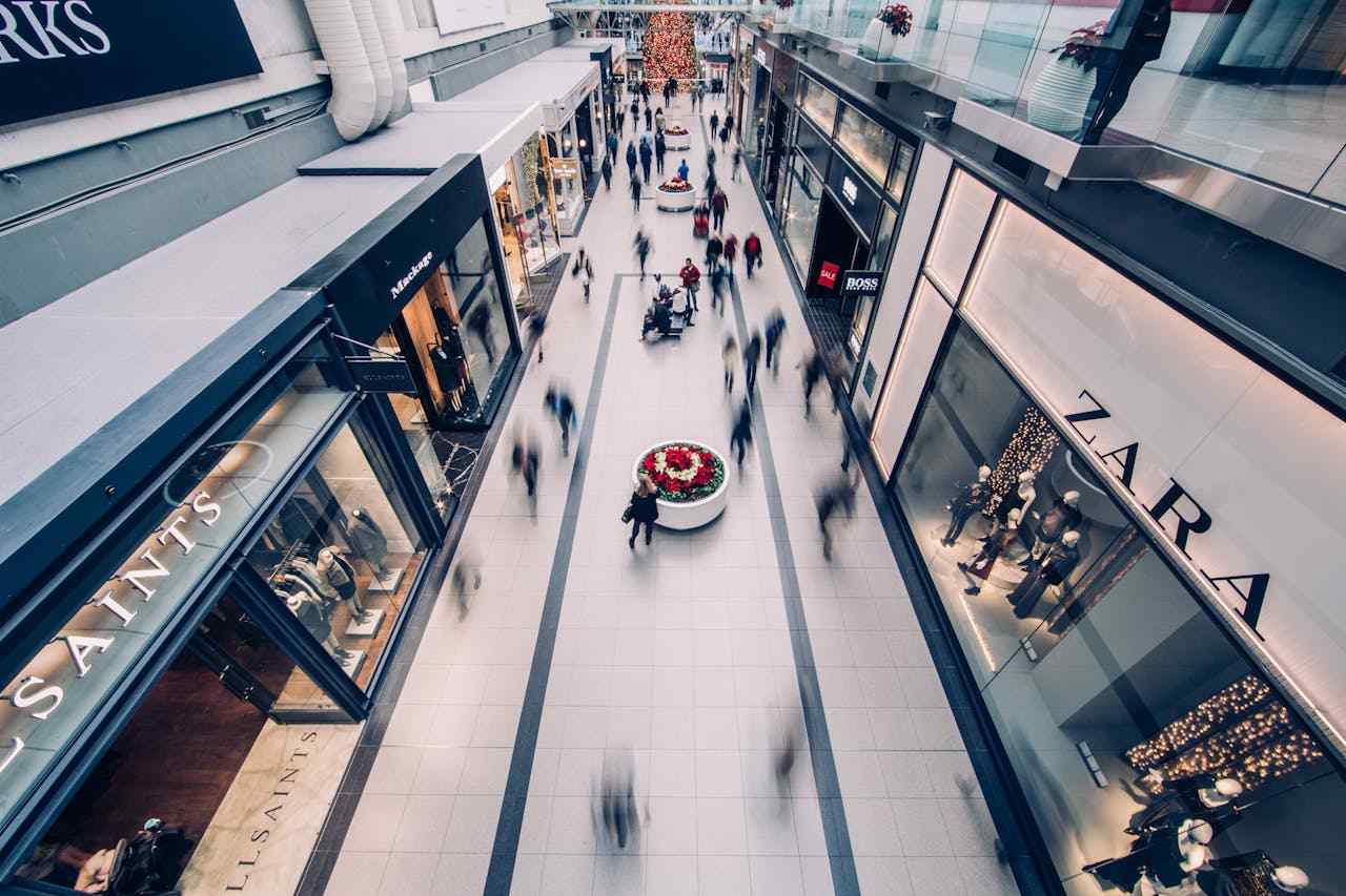 An image of a modern shopping center with people passing by multiple retail stores on their left and right