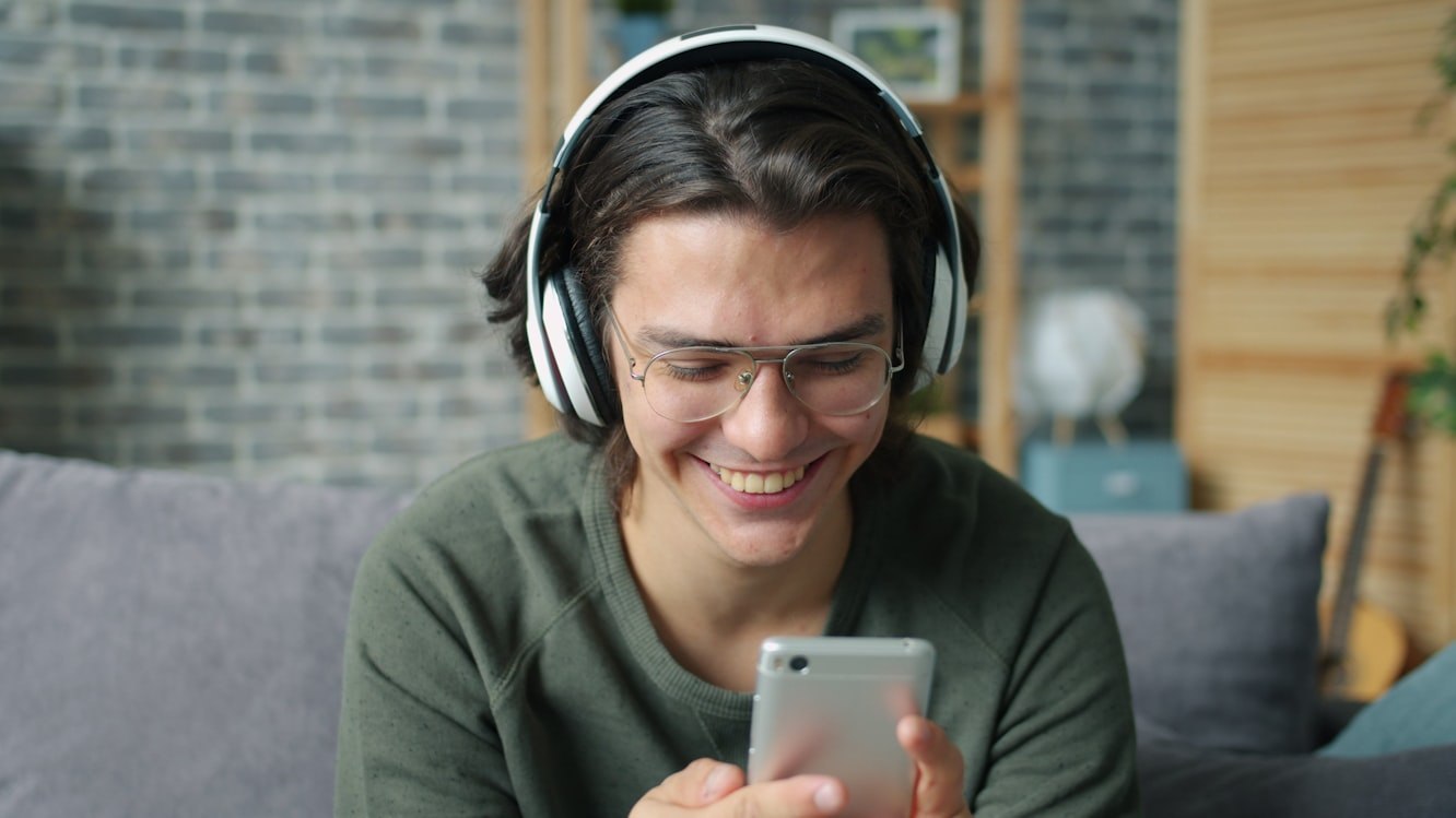 A person with headphones on smiling at their phone
